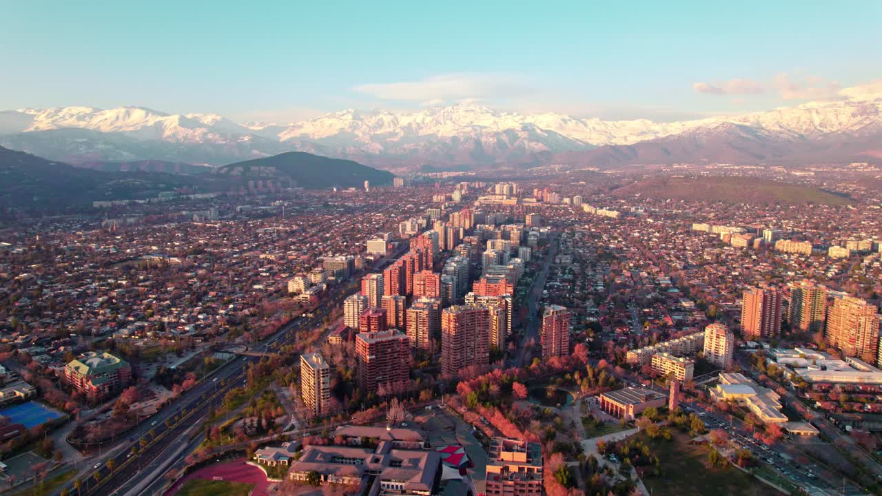 Carrellata aerea degli edifici del quartiere Las Condes, montagne innevate sullo sfondo al tramonto, Santiago, Cile.