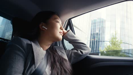 business chinese woman driving in a taxi and using earphones