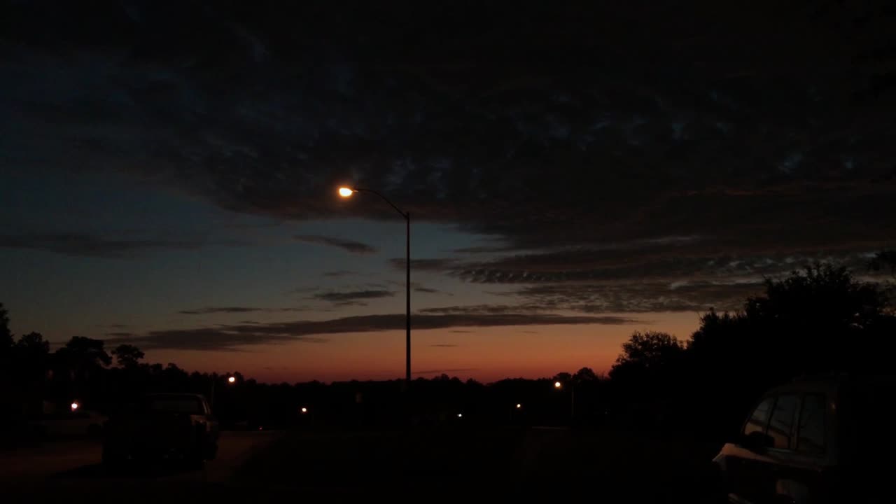 Sunrise in streets of a suburban neighborhood with street lights and parked cars.