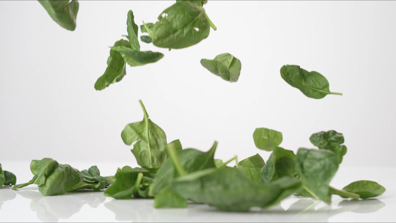 Foglie di spinaci freschi e verdi che rimbalzano su un tavolo bianco al rallentatore, in primo piano macro, prima di posarsi