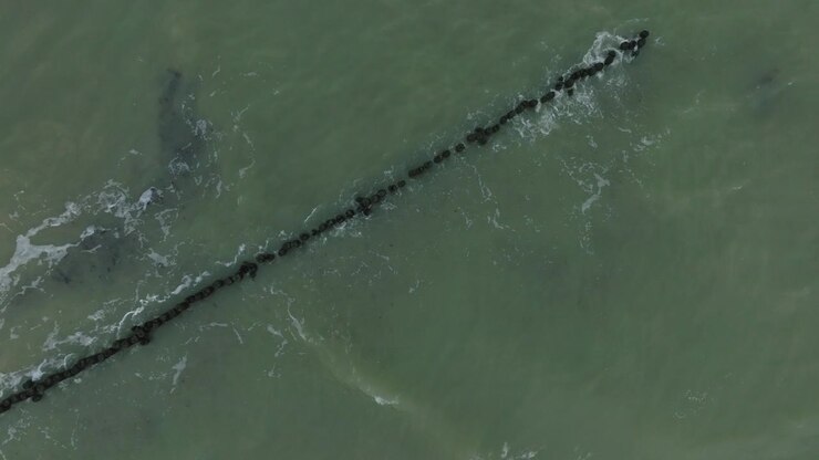 Aerial birdseye view of an old wooden pier at the Baltic sea coastline, overcast winter day, white sand beach, wooden poles, waves hitting shore, wide drone dolly shot moving left