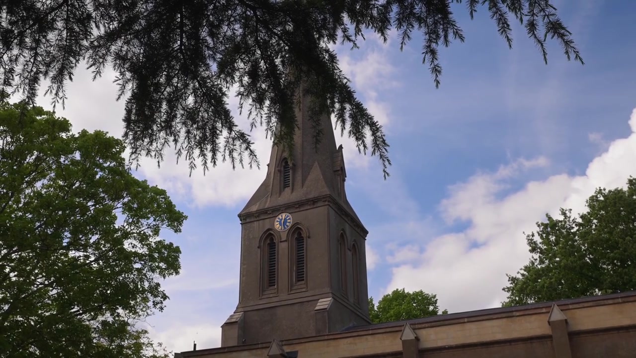 Il campanile della Chiesa di San Leonardo si erge contro un cielo parzialmente nuvoloso, incorniciato da rigogliosi rami verdi di alberi. Ideale per documentari storici o servizi sull'architettura.