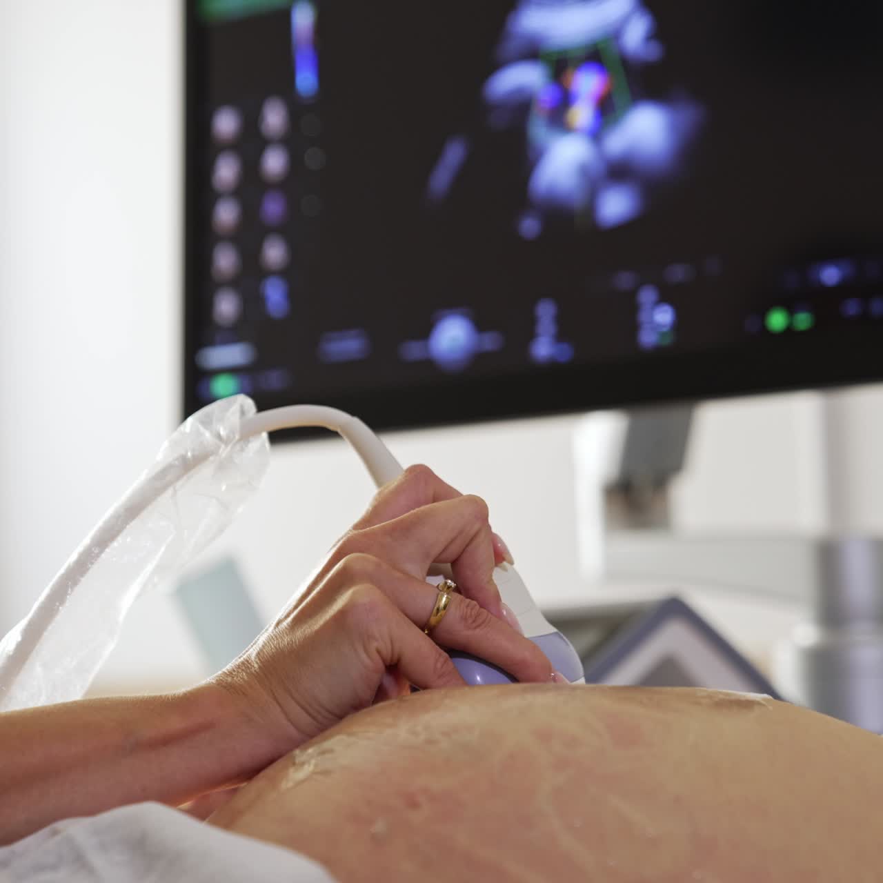 Female doctor's hand moving the sensor by the big pregnant belly. Black screen of a sonographer at backdrop in blur