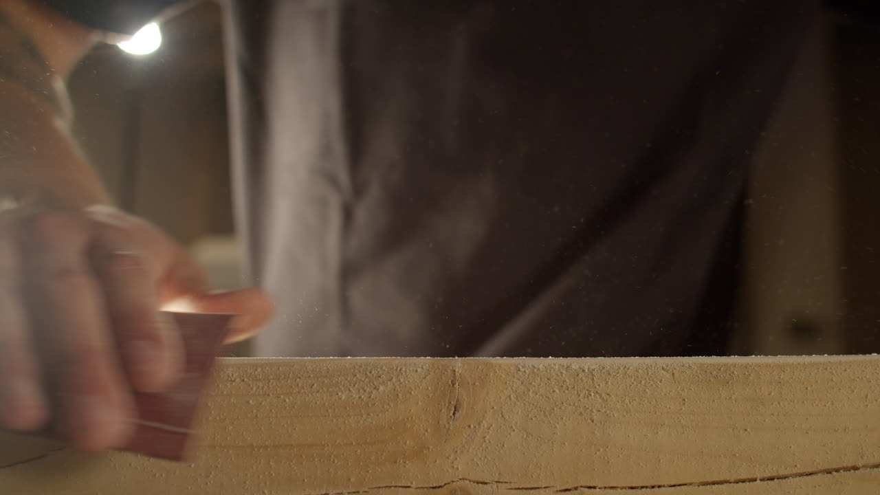 High quality video showing a craftsman sanding a wooden board in warm light with slow smooth hand movements and fine dust in the air creating a rich tactile workshop atmosphere