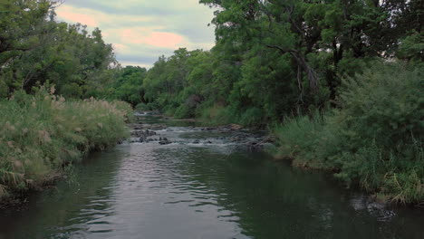 calm peaceful scene of slow flowing river over rocks- low flying drone shot