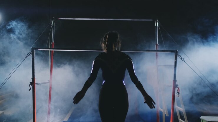 Competitions in gymnastics. A woman walks to the crossbar and performs dips flip-flops in slow motion on a dark background in backlight. Slow motion.