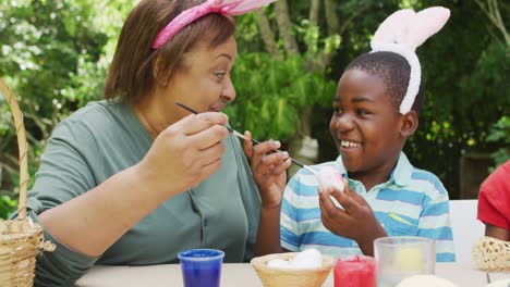 Animation-of-happy-diverse-grandmother-and-grandson-painting-easter-eggs-in-garden