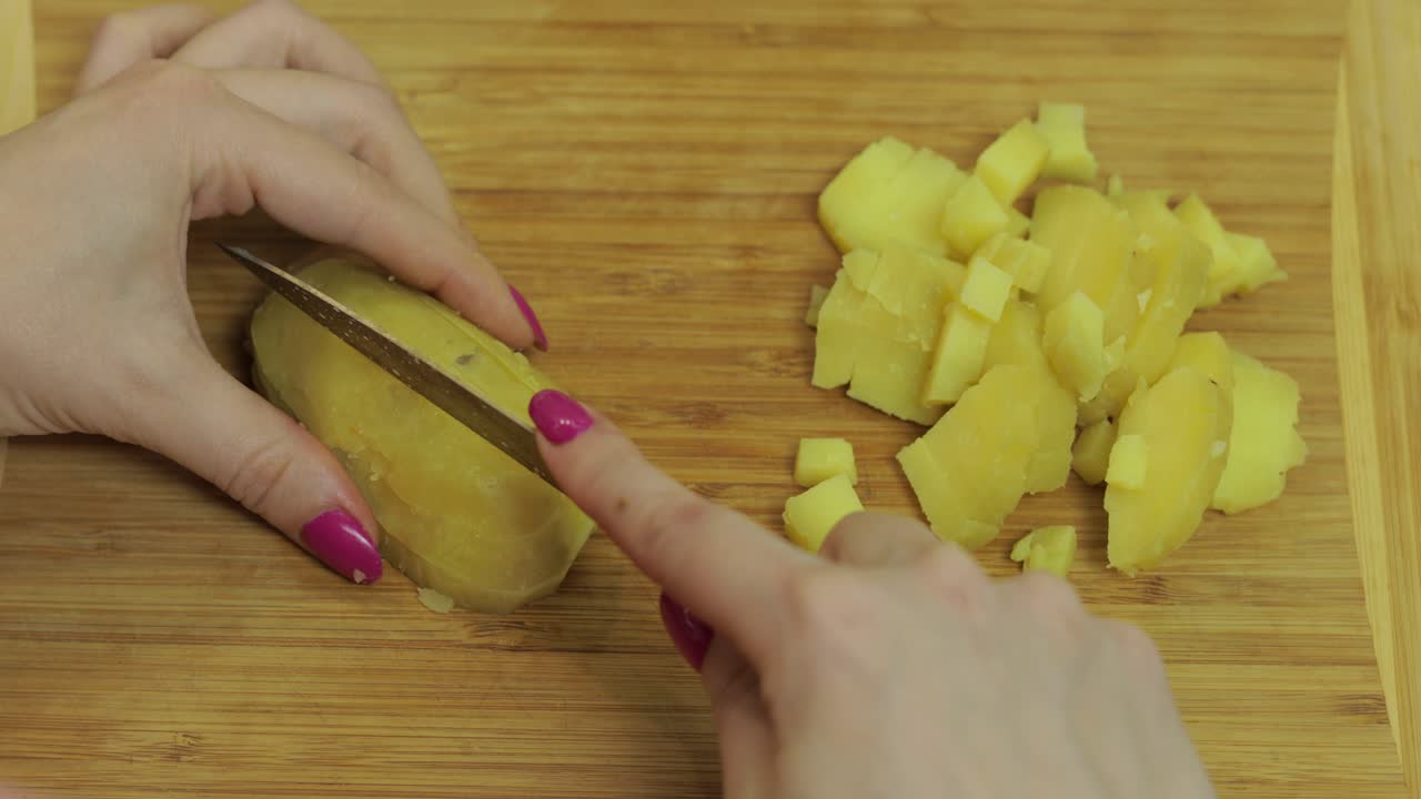 las manos de la ama de casa cortando patatas en pedazos en la cocina