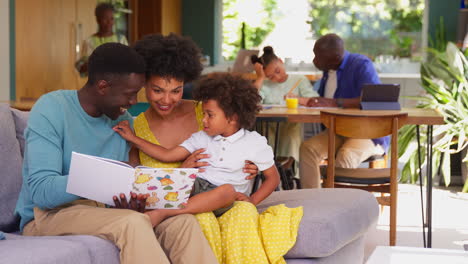 multi-generation family with parents reading book to son and grandfather helping granddaughter