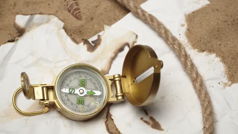 man hand putting gold compass on burnt maps on sand background close-up, golden compass in human palm. traveling and tourism concept, navigation