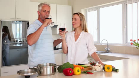 happy couple drinking red wine together while making dinner