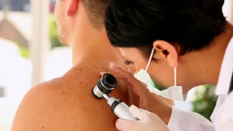 hombre que recibe su lunar revisado por el dermatólogo