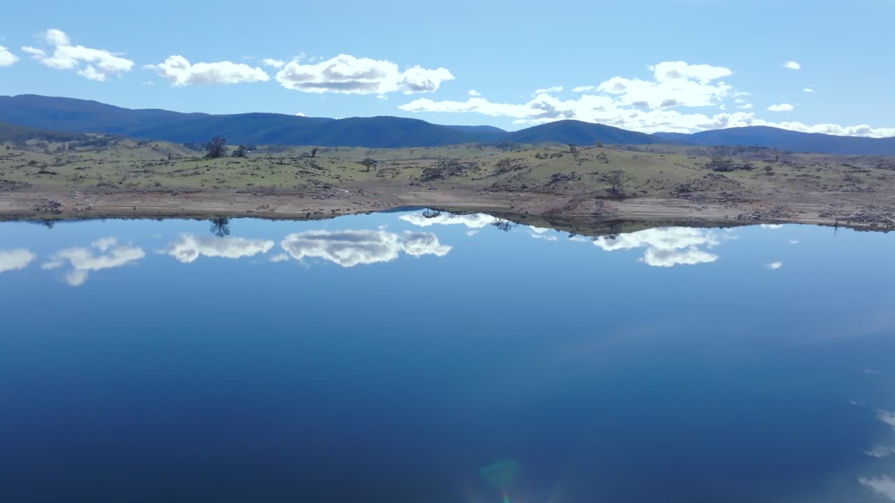 Drone shot over Lake Jindabyne shows white clouds reflected in the water