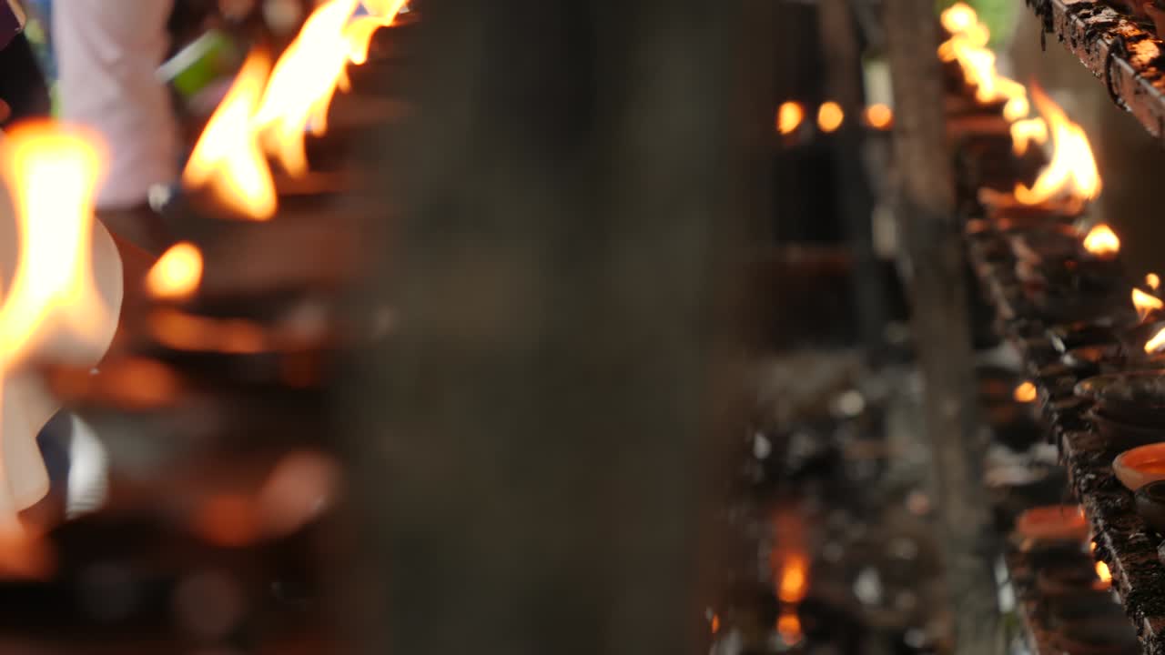 CLoseup dolly video of worshippers lighting up burning oil lamps with sacred fire at buddhist temple