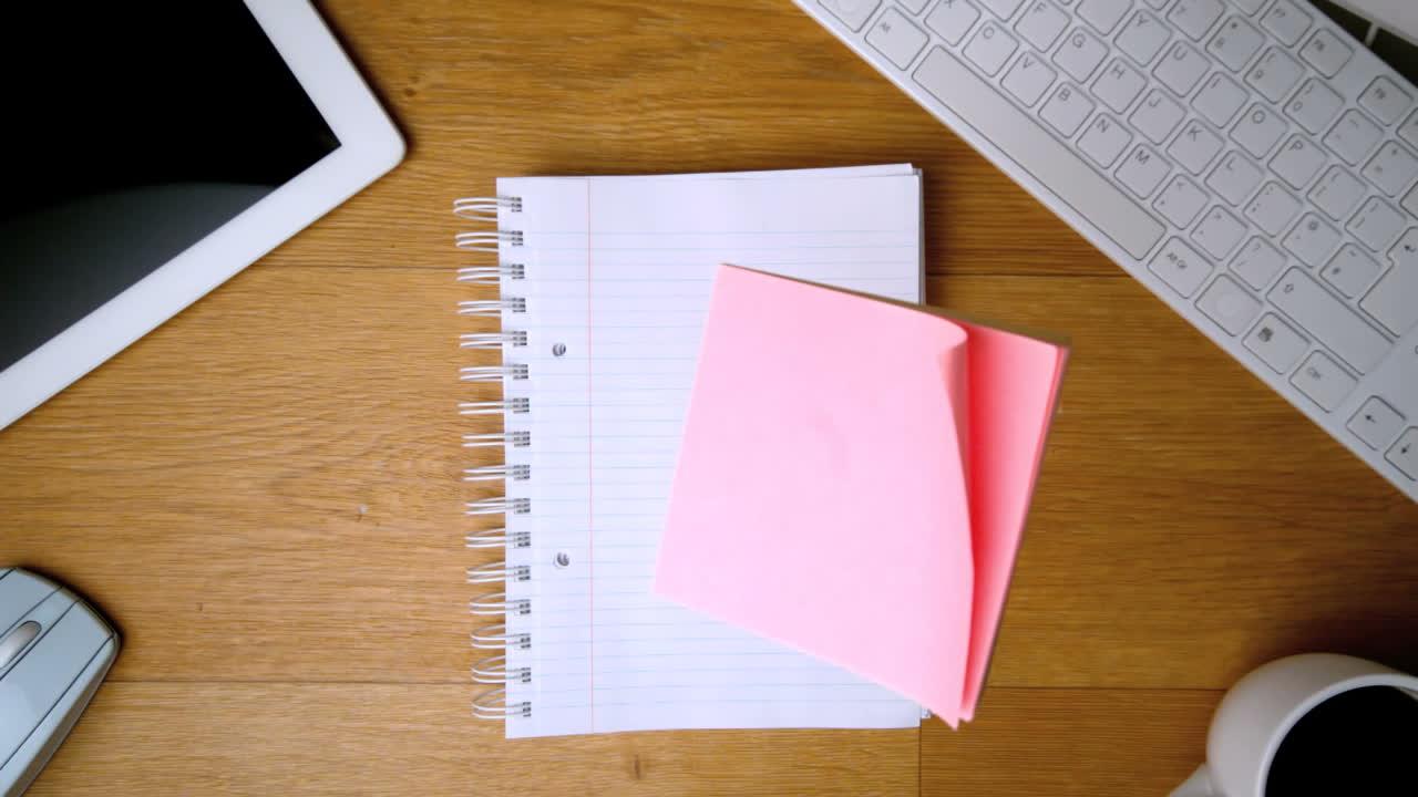 Pink post its falling on notepad on office desk