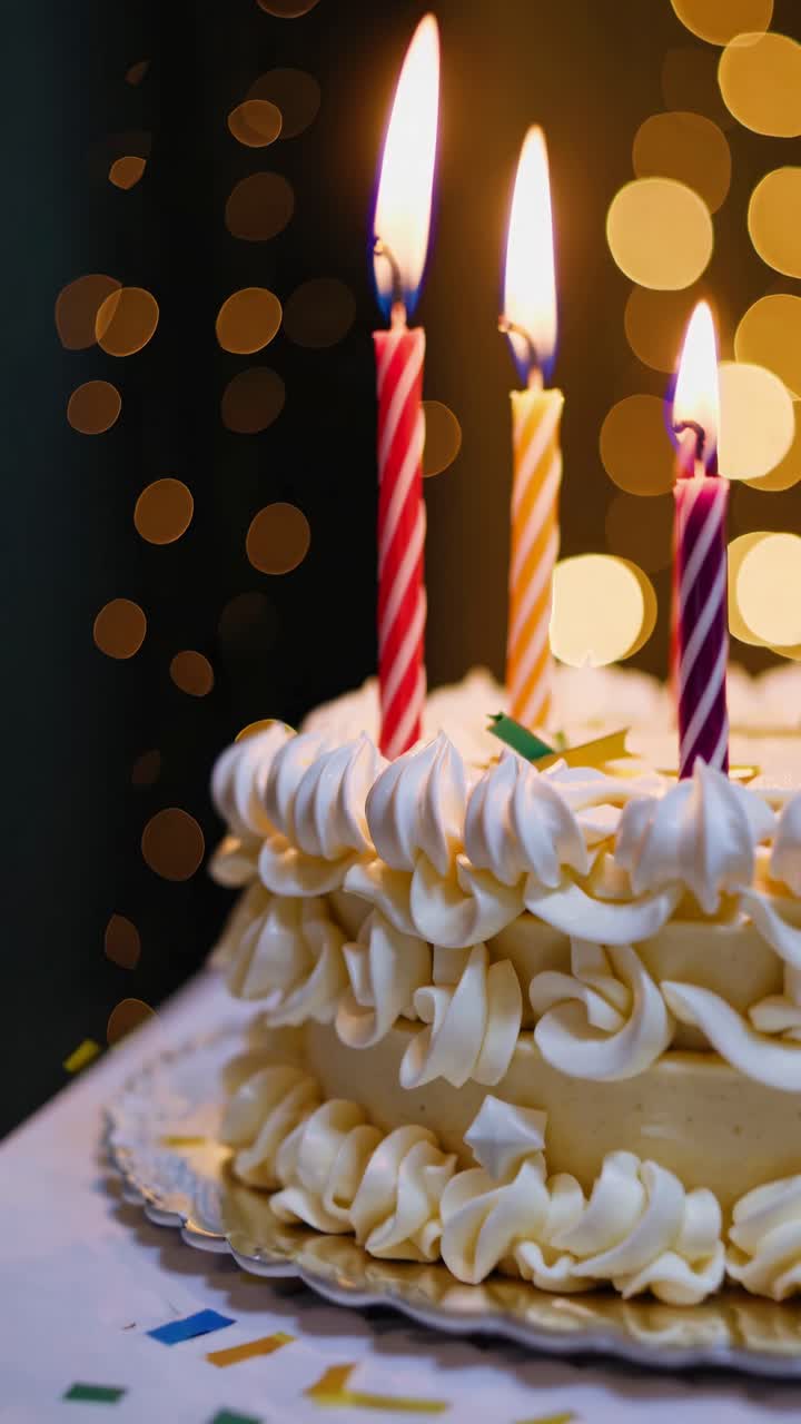Close-up video angle of a festive cake with lit candles, surrounded by colorful confetti and warm