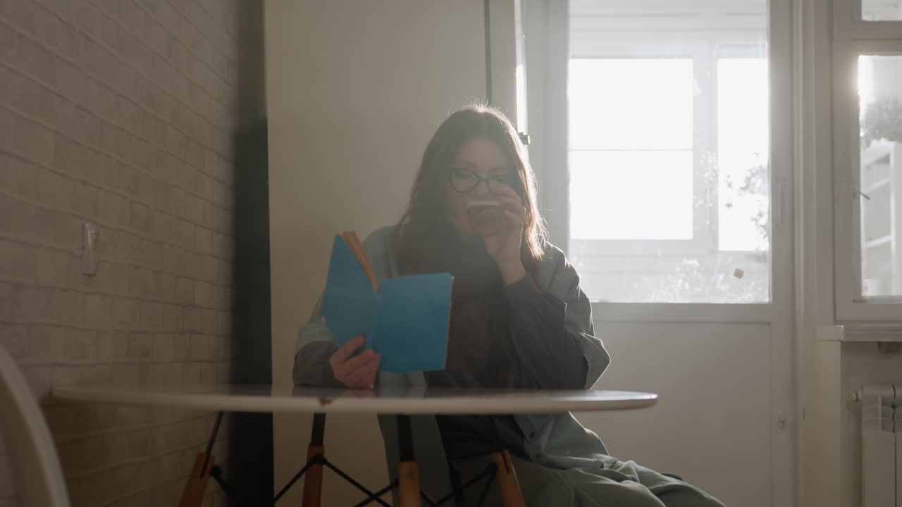 Donna serena assorta nella lettura e nella scrittura. Donna che si concentra sul lavoro in un ambiente di cucina moderna e luminosa. Scena tranquilla di una donna immersa nei suoi studi con una tazza di tè in una cucina ben illuminata.