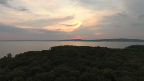 Drone-flying-sideways-over-forest-before-continuing-over-water-at-dawn