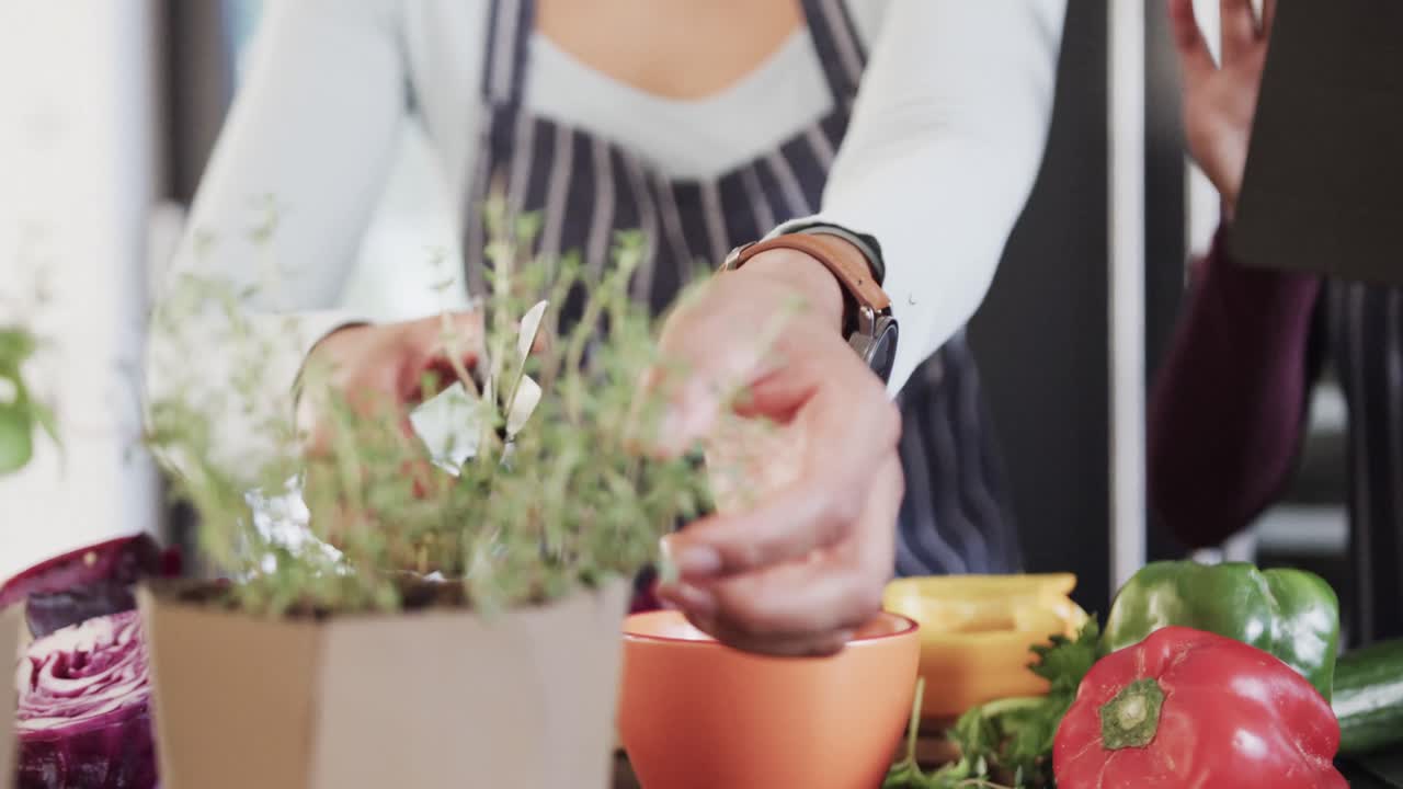 두 인종의 레즈비언 커플이 부 ⁇ 에서 약초를 자르고 태블릿을 사용하여 느린 움직임을 보입니다.