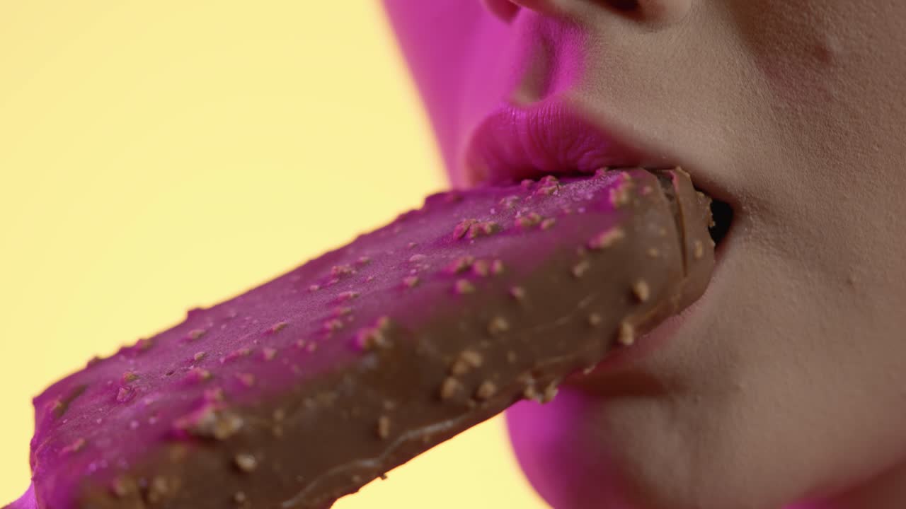 한 초콜릿 맛의 팝시클 아이스크림을 먹는 여성의 입을 가게 찍은 다채로운 스튜디오 촬영