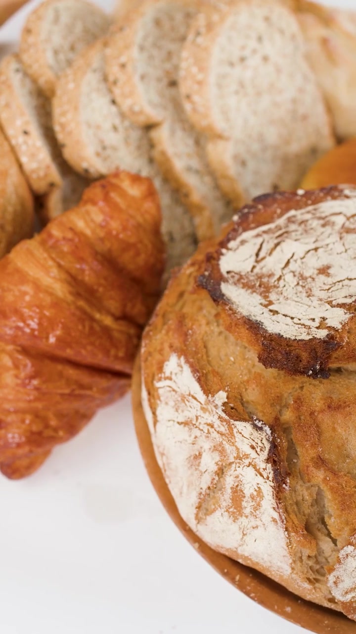 Slow panning shot across sourdough loaf, croissant, baguette, and sliced whole wheat bread.