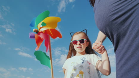 una niña alegre juega un molino de viento de juguete cerca de su madre embarazada