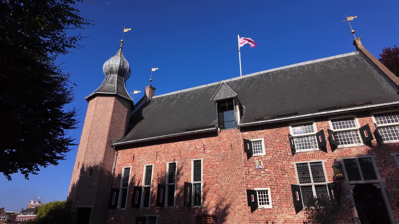 Detailed view of a red brick courthouse tower with Dutch flag waving against a clear blue sky. Location: Coevorden, Drenthe, Netherlands (Coevorden, Drenthe, Nederland)
