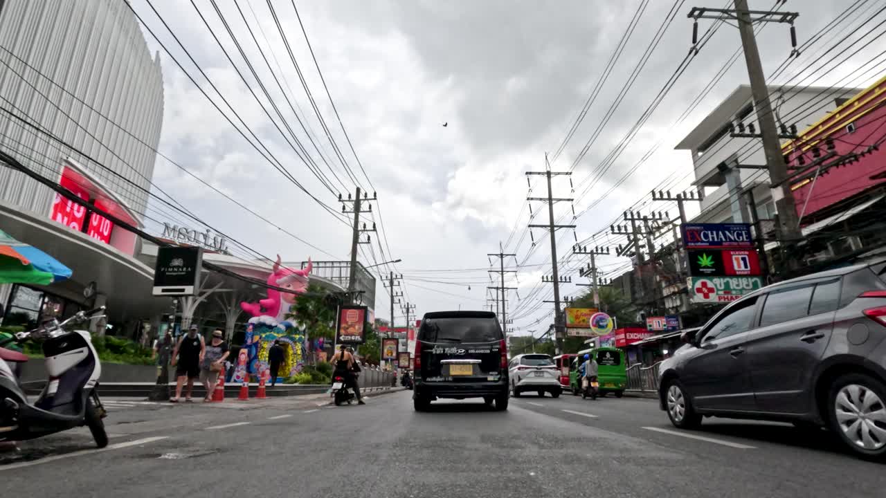 Vehicle moves along lively Phuket street with shops, pedestrians, overcast daylight, and steady camera