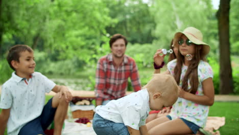Small-toddler-popping-bubbles-in-park-with-family-on-background