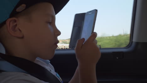 Kid in the car taking cell photos of city street