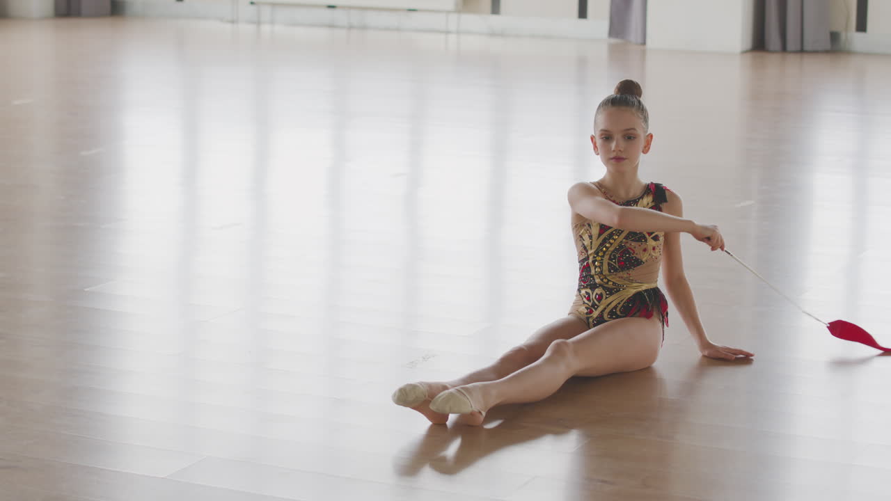 niña en leotardo practicando gimnasia rítmica con una cinta en un estudio 3