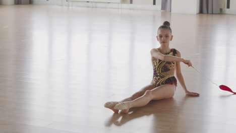 young girl in leotard practising rhythmic gymnastics with a ribbon in a studio 3