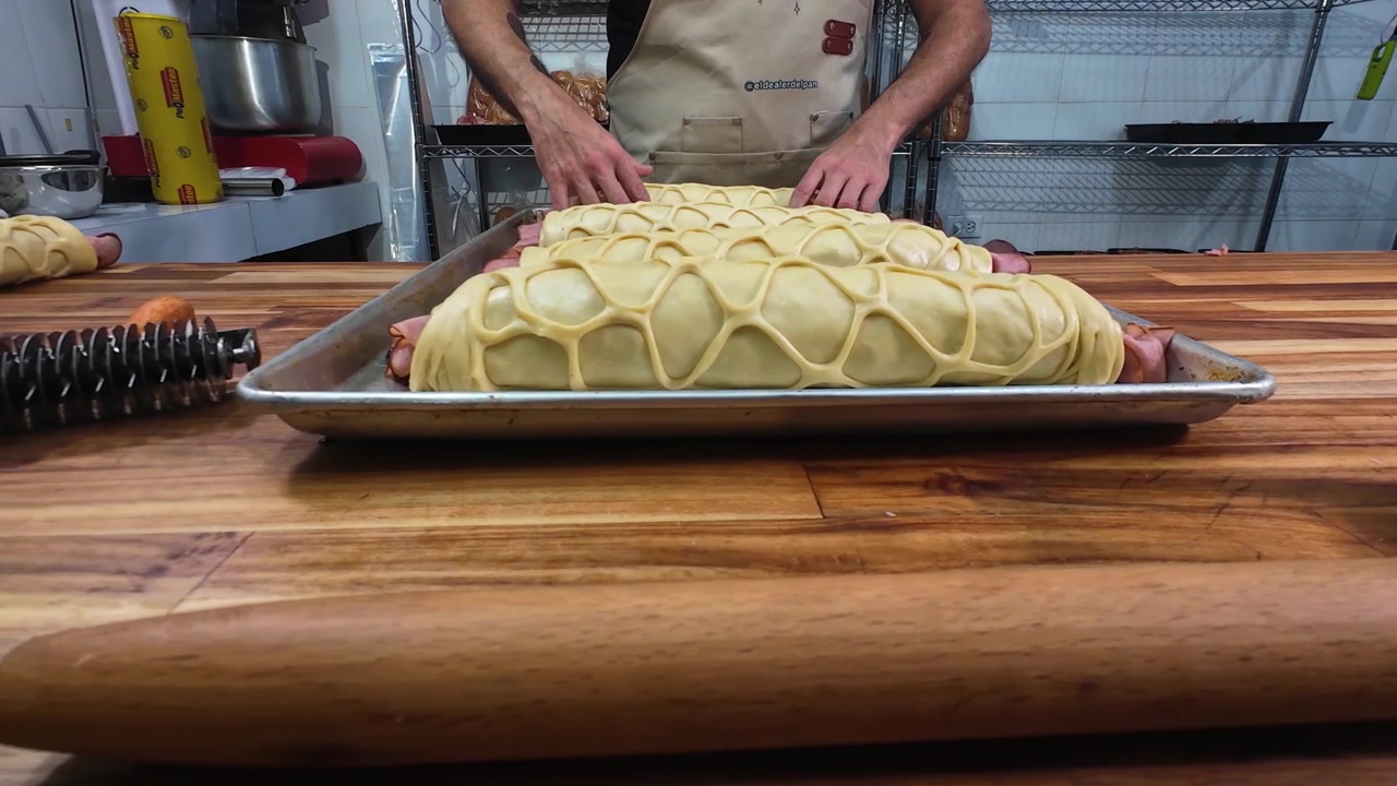 Close-up baker carefully positioning handcrafted pan de jamón with decorative lattice dough onto commercial baking tray before baking. traditional Venezuelan holiday bread is prepared by hand