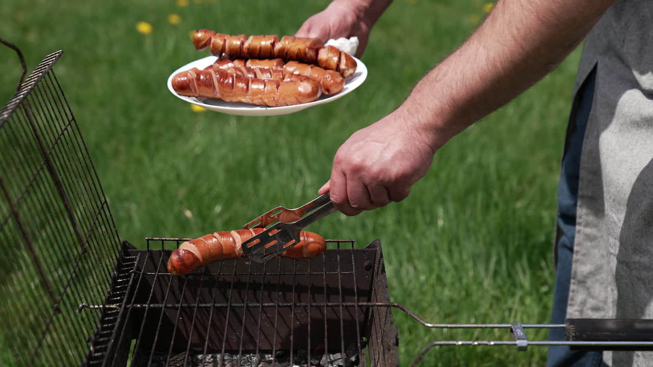 Man on picnic prepares juicy sausages in barbecue. Chef putting ready roasted hot dog sausages into a plate in the garden.