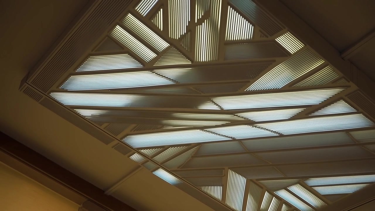 Telecamera a mano che si inclina, mostrando un lucernario su un soffitto pubblico e rivelando le doghe di rifinitura nell'angolo inferiore destro.