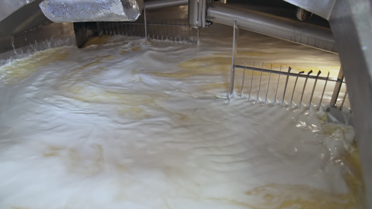 Automatic mixing of fermented milk with two big nozzles in wide tank. Process of cheese production at milk factory. Close up.