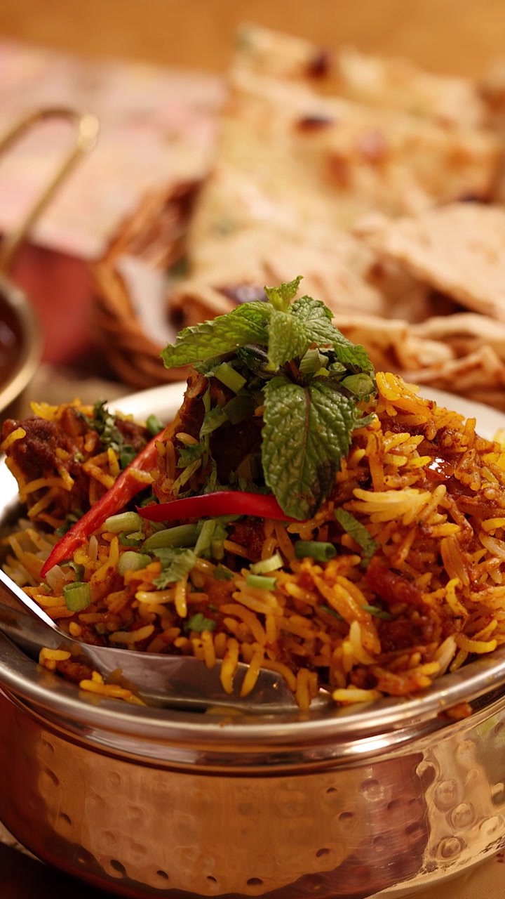 Nærbillede af krydret kyllingebiryani i en metalskål med naan og yoghurtsauce