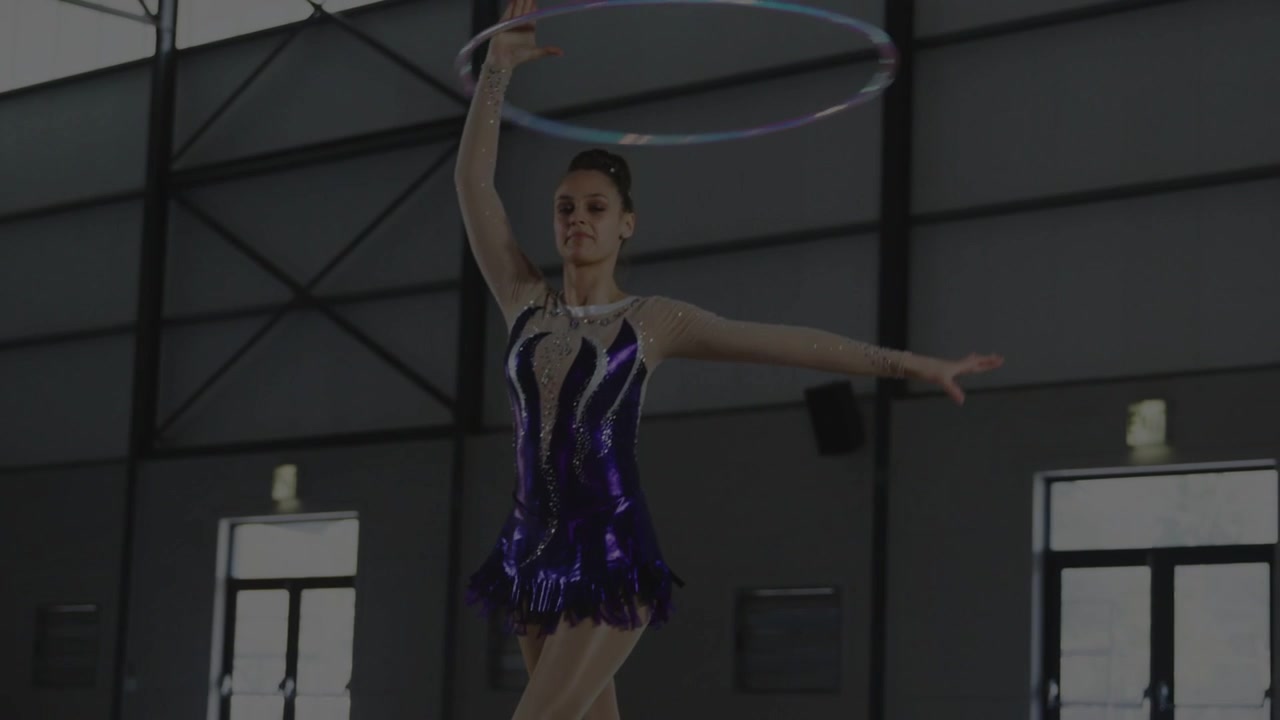 Ginnasta che si spinge dal pavimento, alzandosi e guidando un cerchio intorno alla testa mentre esegue una routine sportiva.