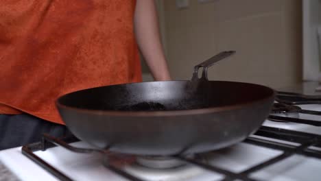 man turns on the gas stove and then puts the frying pan over the fire in the kitchen