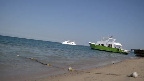 people walking into a parked green boat while white ship sails behind, still, slomo