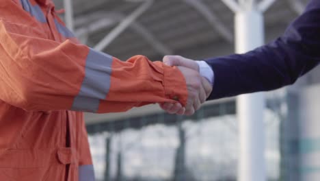 professional worker in orange uniform shaking hands with businessman in a suit. close up view