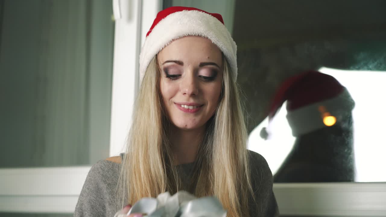 Friends exchanging Christmas present. Young women playing Christmas gift exchange on window sill at home