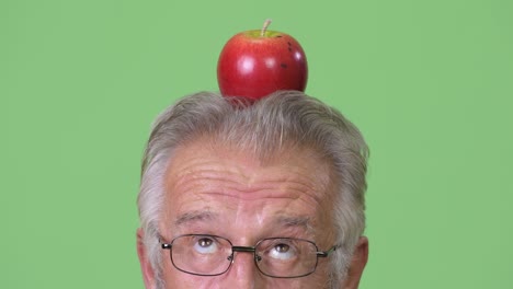 head shot of senior man with apple on top of head against green background