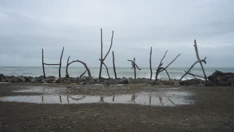 wooden sign of hokitika, west coast, new zealand. built out of branches. waves breaking in the background on this stormy day