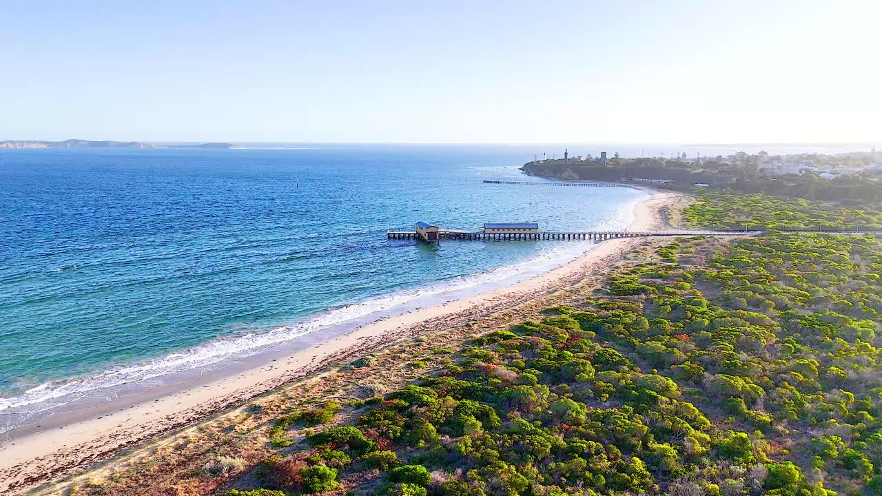 Drone footage captures Bellarine Peninsula's coastline with lush greenery, sandy beaches, and a tranquil pier under bright daylight