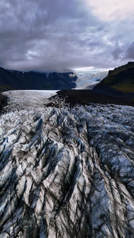 unapproachable ridged surface of ancient glacier of white, black and grey colors. iceland landscapes from drone. low angle view at the dramatic cloudscape covering the mountain tops and sky. vertical video.