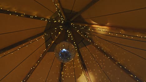 party tent interior with disco ball hanging and reflecting light surrounded by led fairy lights. 50 fps slow orbit and rack focus.