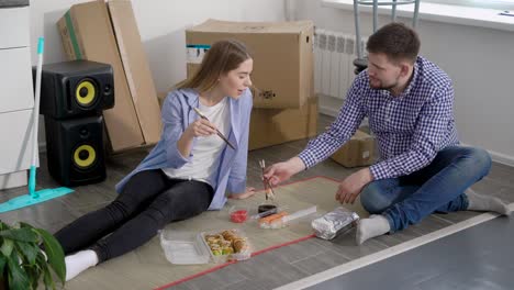 young man and woman celebrating the move in and eating sushi while sitting on floor