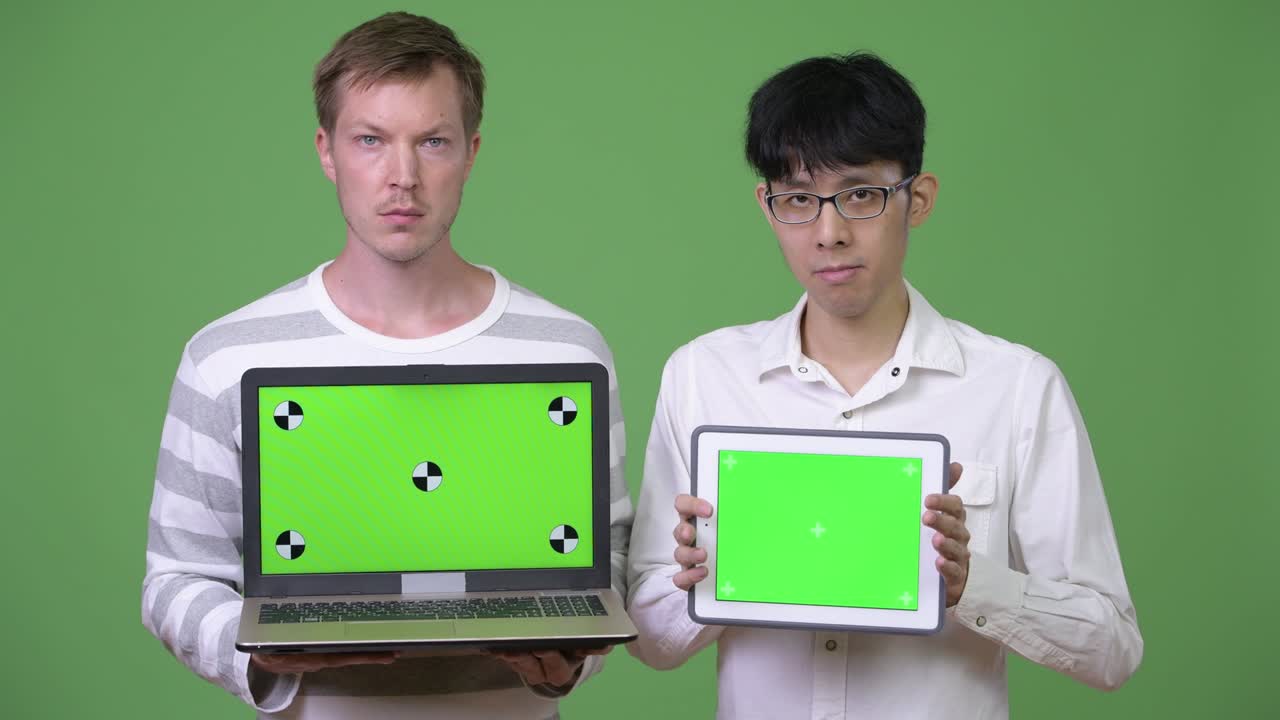 dos jóvenes empresarios multiétnicos mostrando una computadora portátil y una tableta digital a la cámara