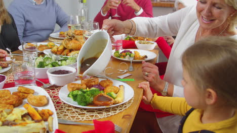 grandmother pouring gravy onto granddaughters food as multi-generation family eat christmas meal